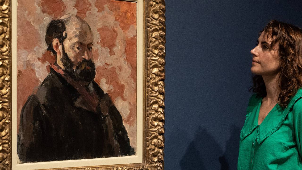 A member of staff examines a painting entitled 'Portrait of the artist with a pink background', by French artist Paul Cezanne at the Tate Modern gallery. /Niklas Halle'n/AFP