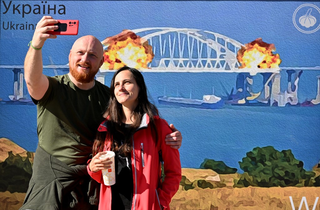 A couple take a selfie in front of a Kyiv artwork depicting Saturday's explosion on Kerch bridge./Sergei Supinsky/AFP