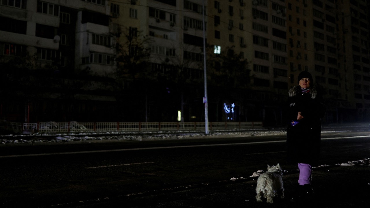 A woman with a dog waits for a bus in a street without electricity after critical civil infrastructure was hit by Russian missile attacks, in Kyiv. /Valentyn Ogirenko/File Photo/Reuters