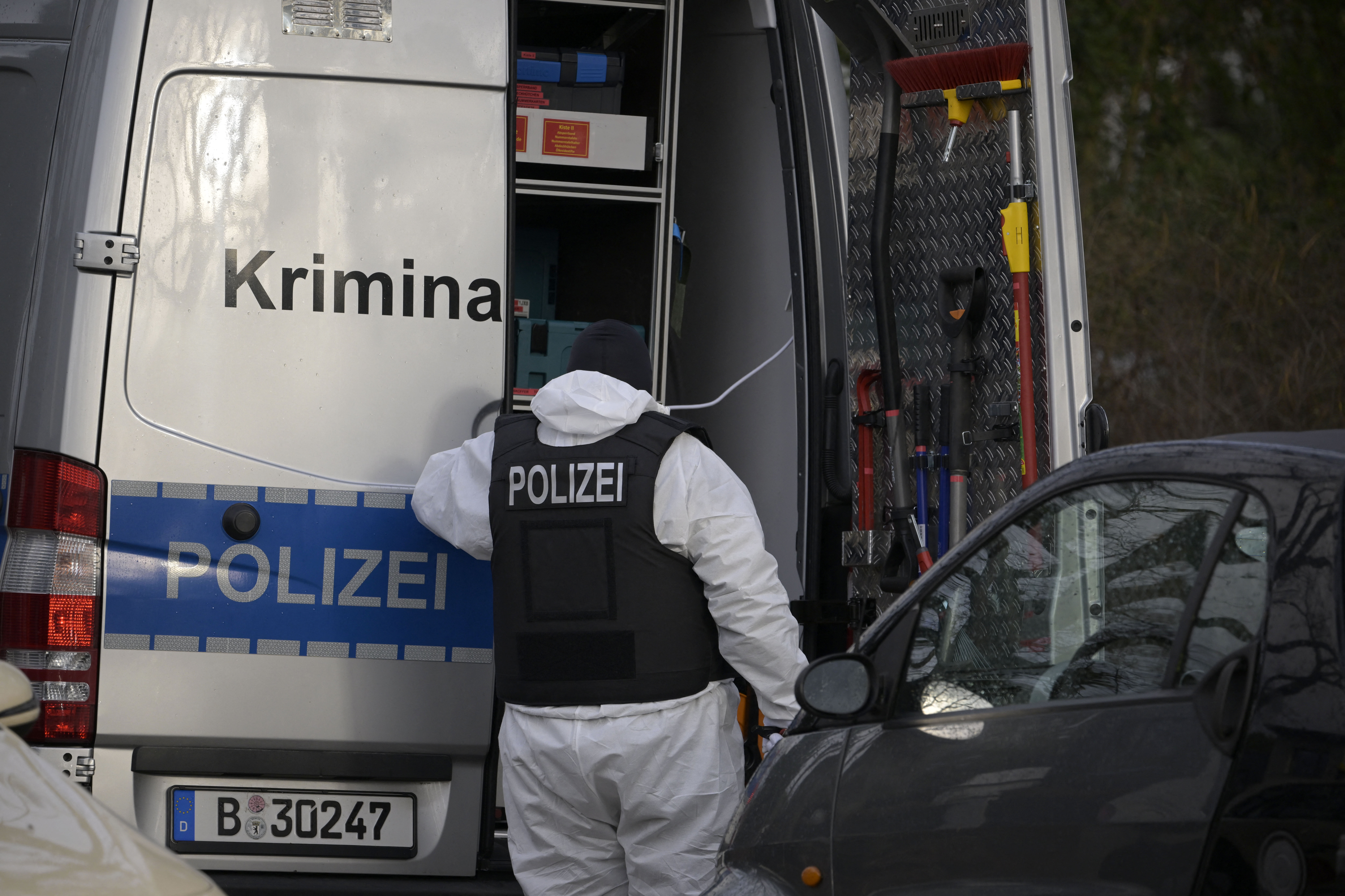 A policeman stands behind a car of the forensic experts during one of the raids  in Berlin. /Tobias Schwarz/ AFP