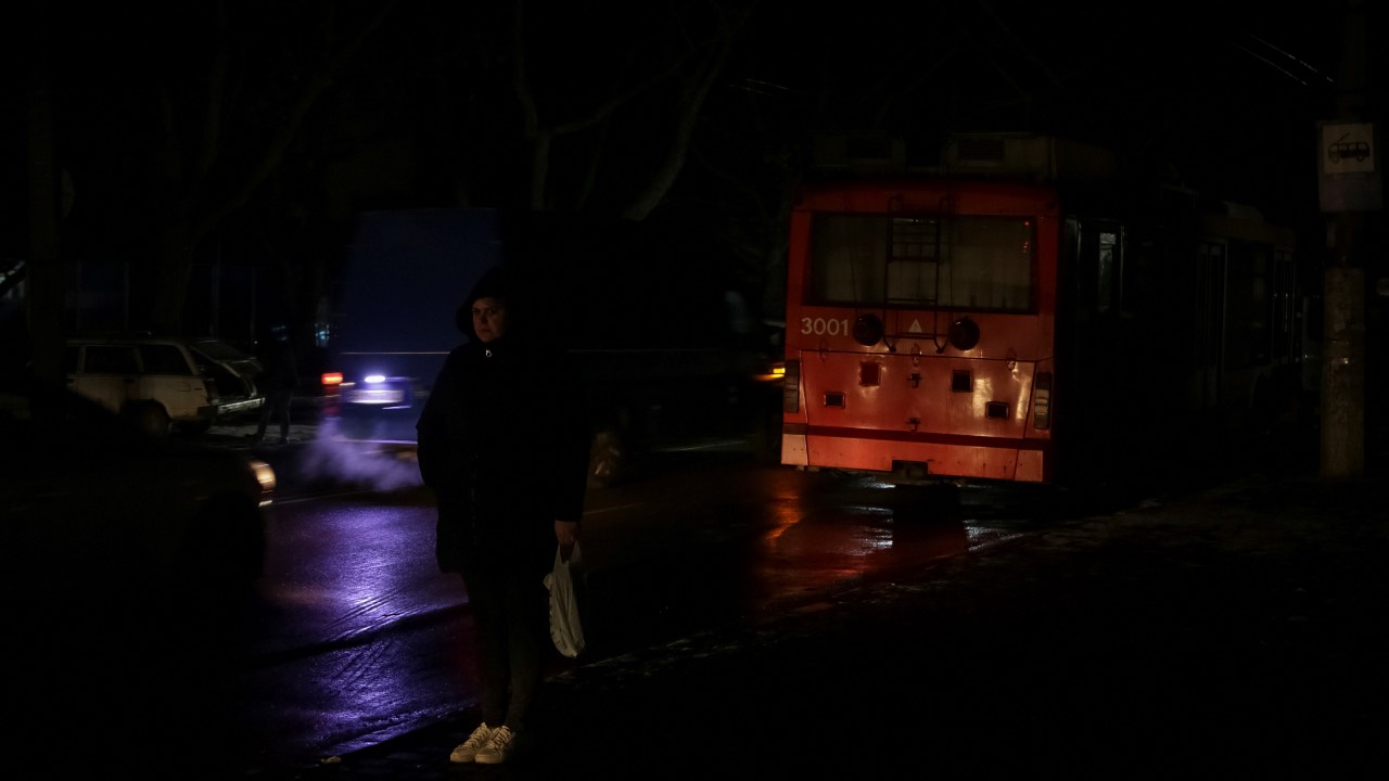 A local resident stands at a transport stop near a stopped bus during a power outage after critical civil infrastructure was hit by Russian missile attacks, in Odesa, Ukraine. /Serhii Smolientsev/Reuters
