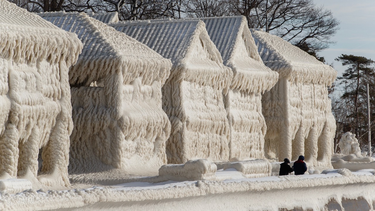 People walk by homes covered in ice at the waterfront community of Crystal Beach in Fort Erie, Ontario, Canada. /Cole Burston/AFP