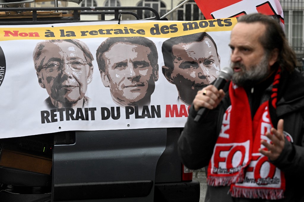 A union leader speaks in front of a banner bearing portraits of France's prime minister, president and labor minister reading 