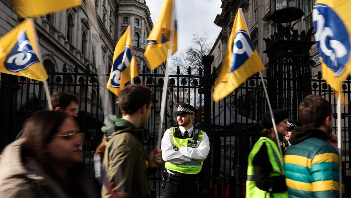 Demonstrators wave flags of the PCS trade union, representing government employees, while marching past the UK prime minister's residence. /Isabel Infantes/AFP
