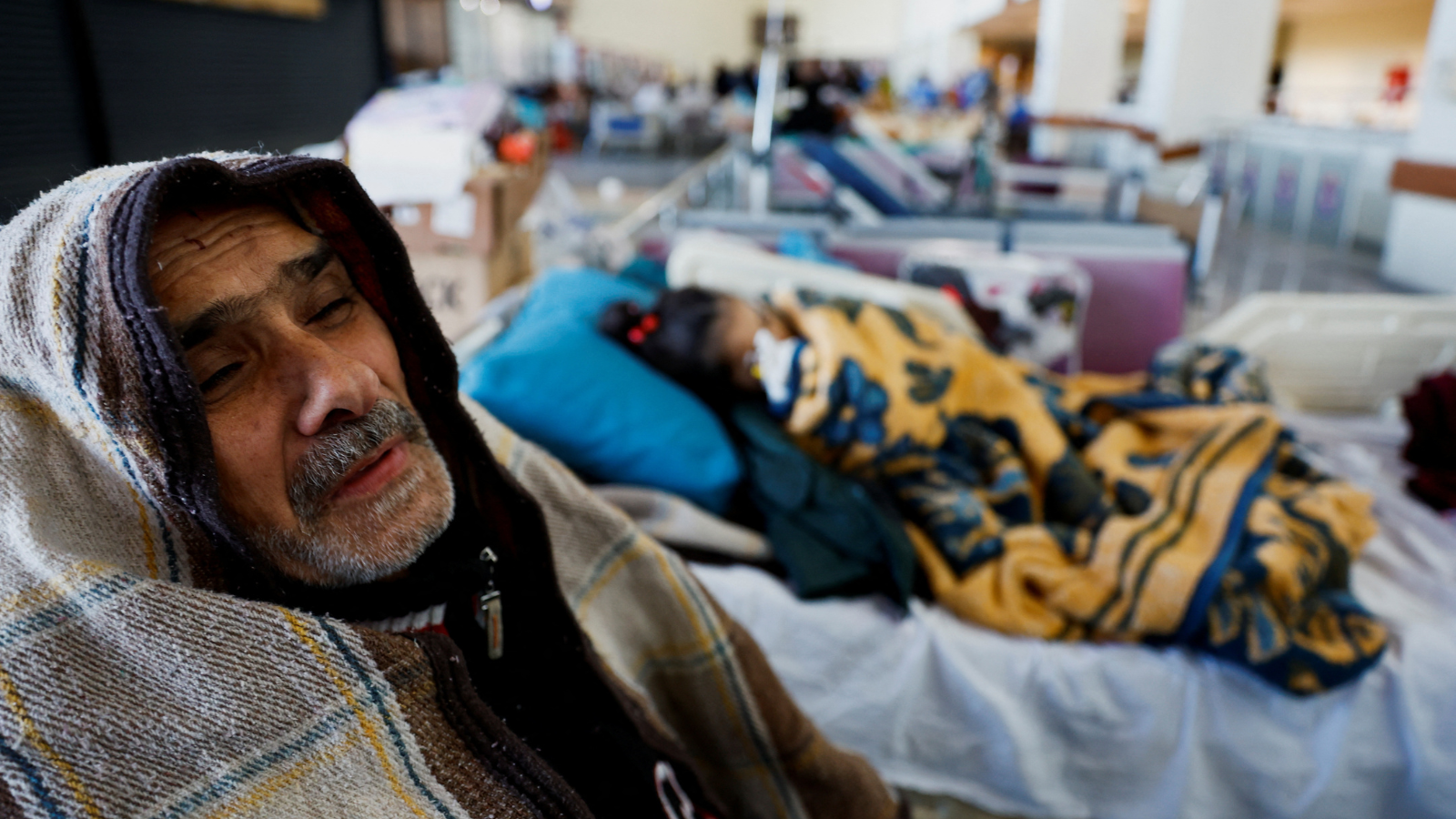 A victim sits next to a child lying in a bed at a hospital in Kahramanmaras, Turkey. /Suhaib Salem/Reuters