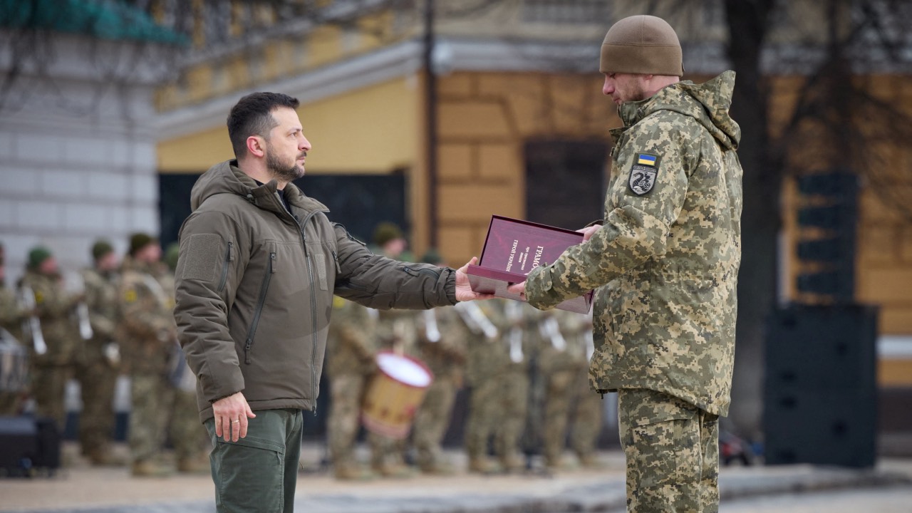 President Volodymyr Zelenskyy hands over a flag to a soldier during a ceremony dedicated to the first anniversary of the Russian offensive in Ukraine. /Ukrainian Presidential Press Service/Reuters
