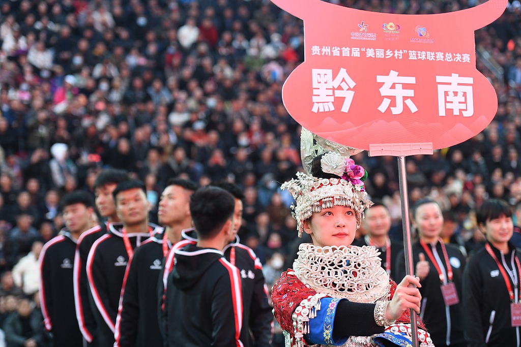 A woman dressed in Miao ethnic clothes holds a board of a basketball team, March 26, 2023, in Guizhou Province. /CFP Photo