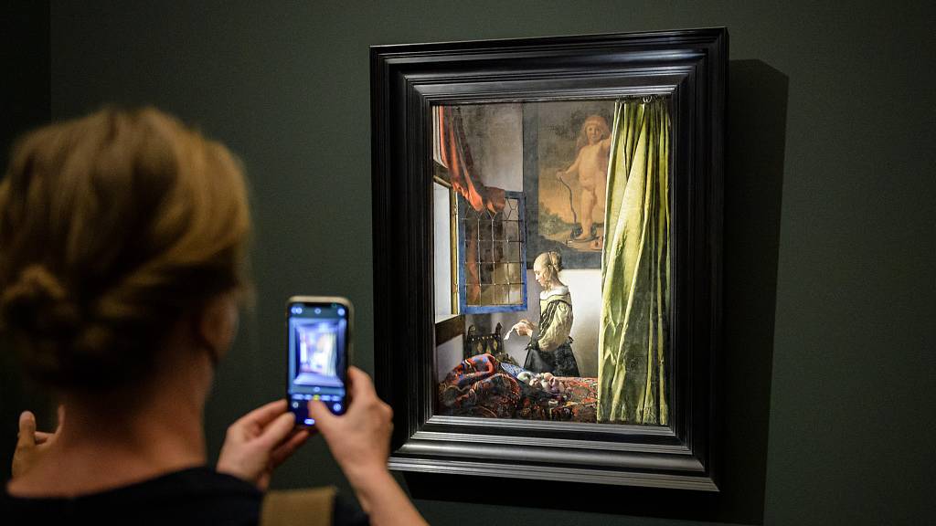 A visitor photographs Vermeer's Girl Reading a Letter at an Open Window at a 2021 exhibition in Dresden, Germany. /Jens Schlüter/ Pool/Getty Images.