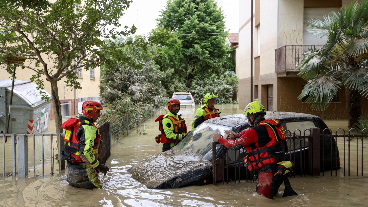 Firefighters work next to a flooded car in Faenza. /Claudia Greco/Reuters