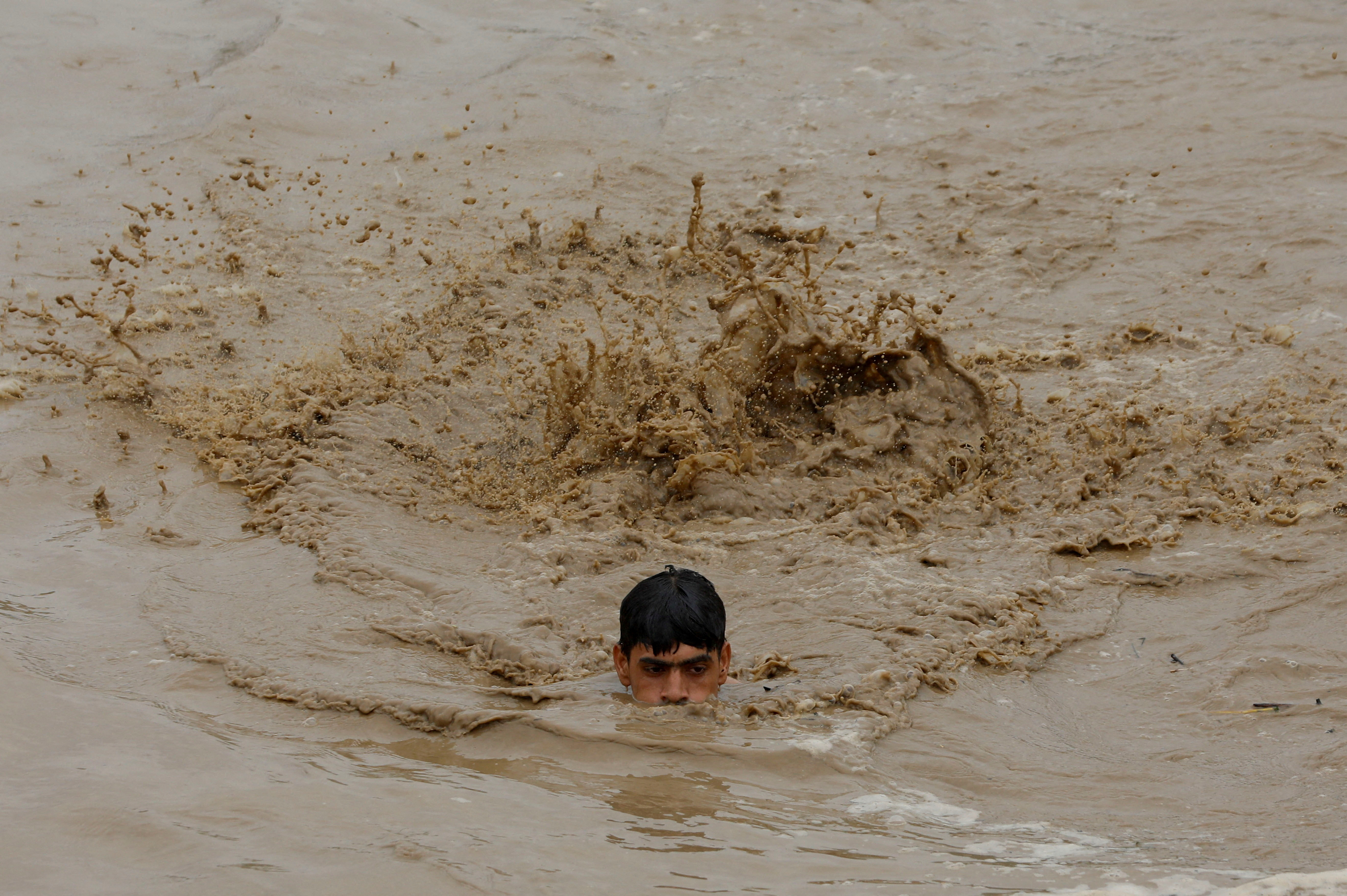A man swims in flood waters while heading for a higher ground, following rains and floods during the monsoon season in Charsadda, Pakistan. /Fayaz Aziz/Reuters
