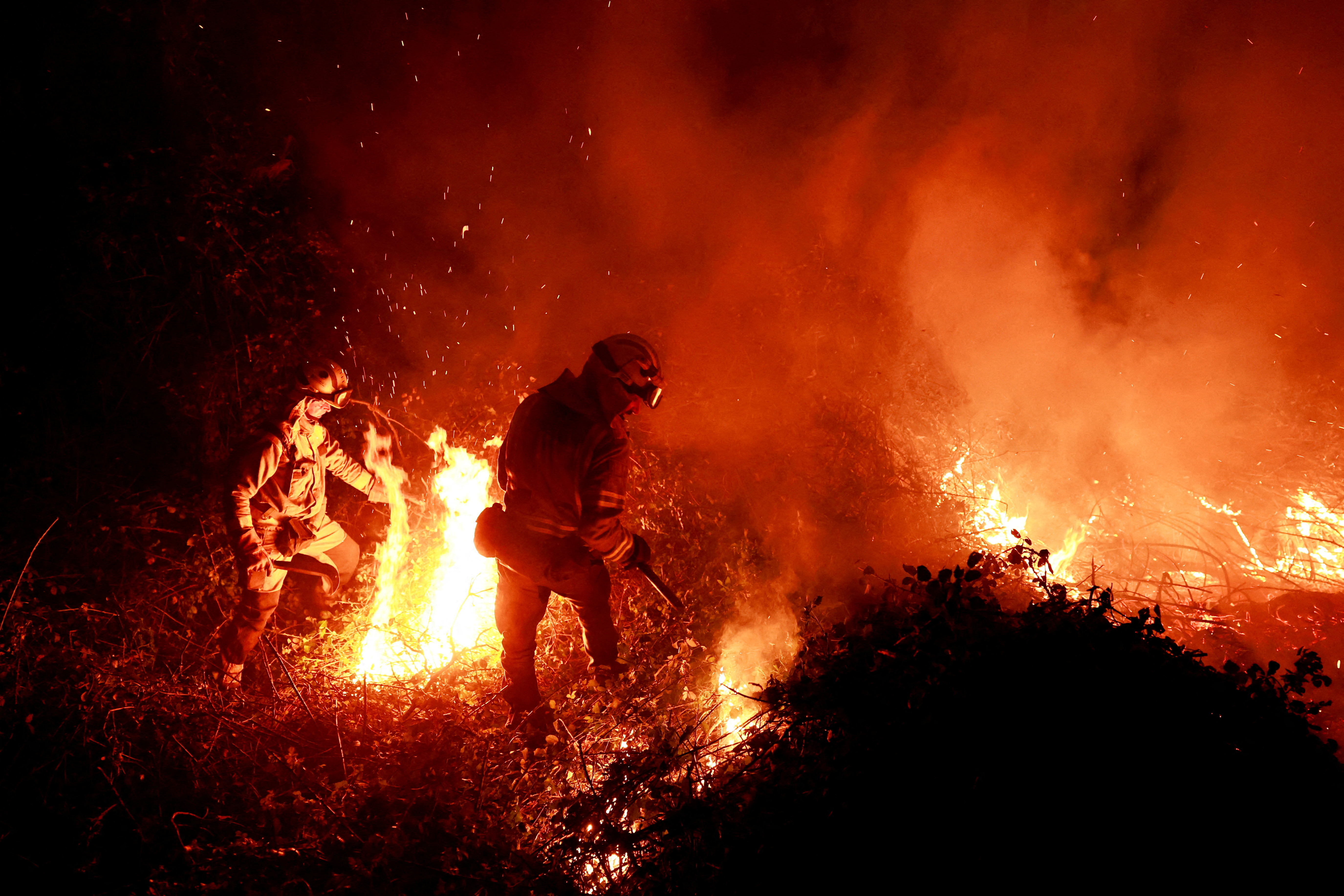 Galician firefighters tackle flames in a forest during an outbreak of wildfires following a prolonged period of drought and unusually high temperatures, in Piedrafita, Asturias, Spain./Reuters/Vincent West.
