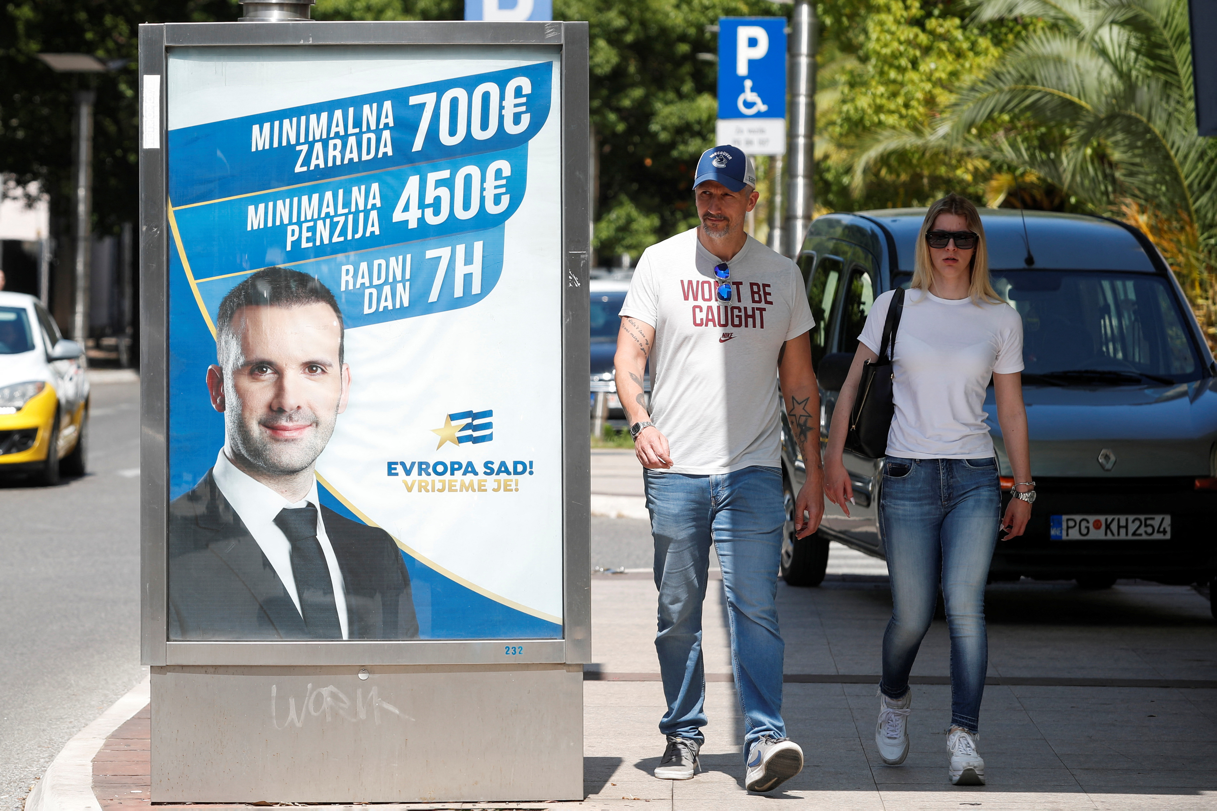 People walk by a campaign poster for election favorite Milojko Spajic as Montenegro prepares for snap parliamentary elections in Podgorica./Reuters/Stevo Vasiljevic.