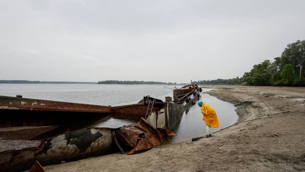 A resident looks at an old barge that became visible on a dried-up river bank after the water level in Dnipro river sharply dropped following the destruction of the Kakhovka dam. /Alina Smutko/Reuters