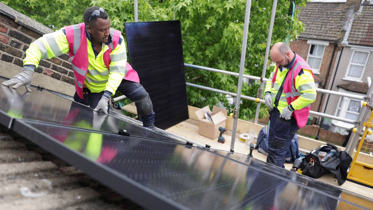 Roofers install solar panels on artists Dan Edelstyn and Hilary Powell's house after the couple raised funds to put similar panels on all the rooftops in their street. /Anna Gordon/Reuters