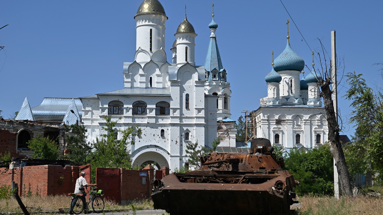 A local resident walks past a destroyed Russian military vehicle and the damaged church in the town of Svyatogirsk, Donetsk region. /Genya Savilov/AFP