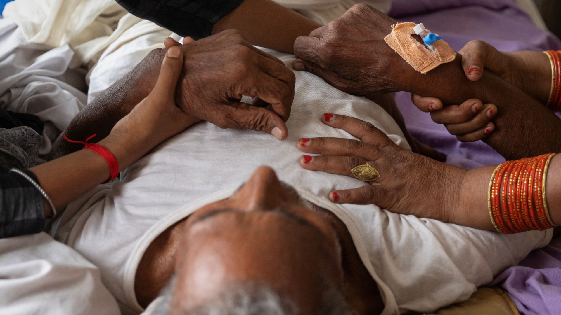 Relatives hold hands of Jagdev Ram, 80, who is suffering from breathing difficulties inside a hospital ward in Uttar Pradesh. /Adnan Abidi/Reuters
