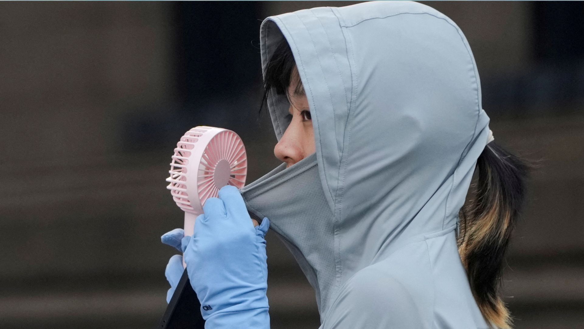 A woman uses a fan as she wears a cloth that protects her from the sun on a street, amid a heatwave warning in Shanghai, China. /Aly Song/Reuters
