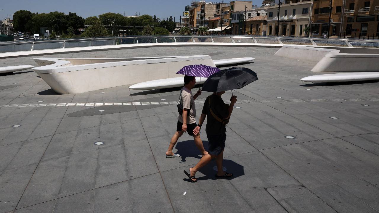 在塞浦路斯尼科西亚的热浪中，男人们撑着雨伞躲避阳光。  /Yiannis Kourtoglou/路透社