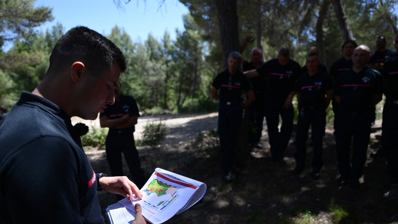 Firefighters listen to the weather forecast as they stand in woods in the Bouches-du-Rhone Department of Marseille. /Christophe Simon/AFP