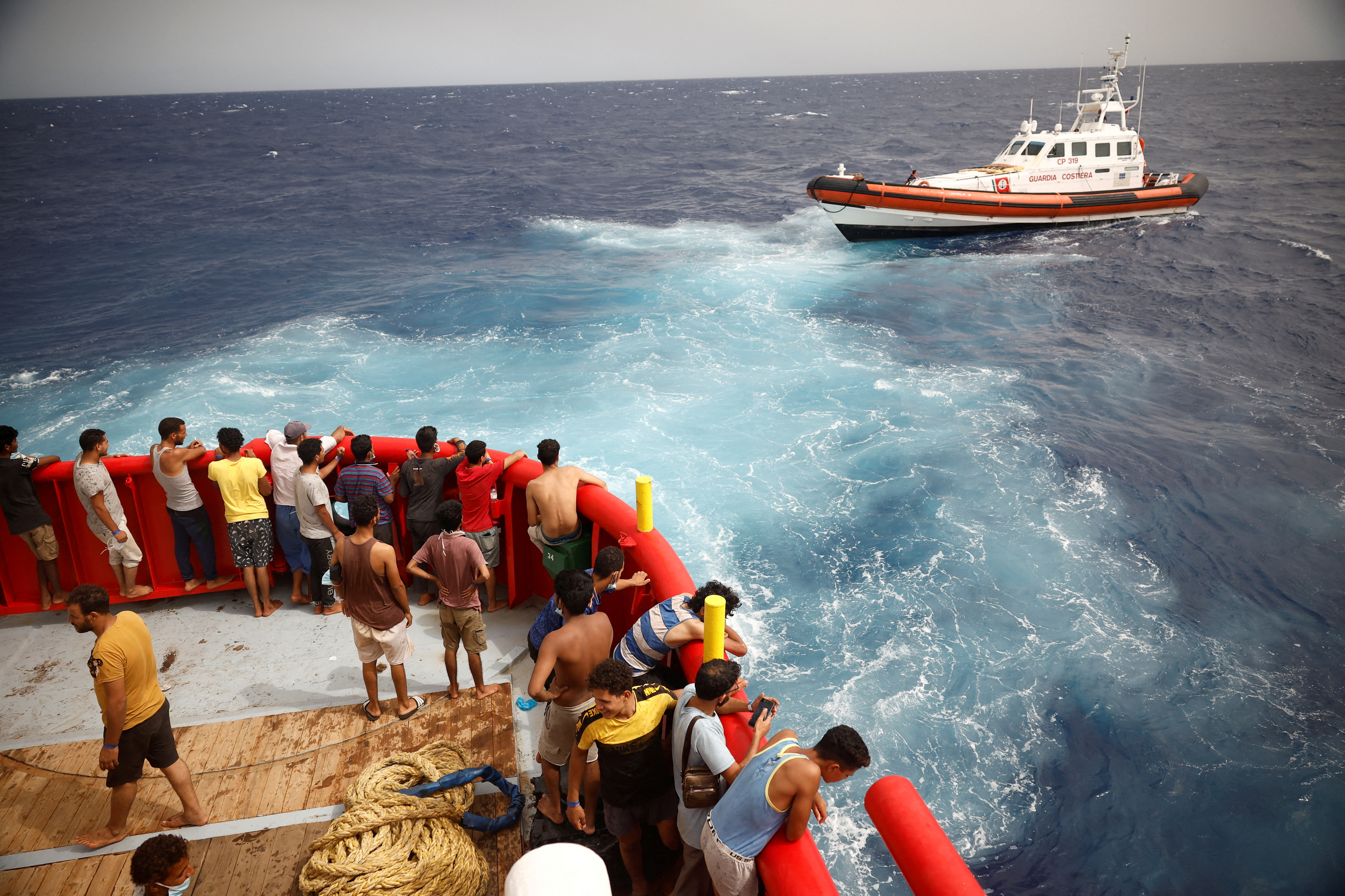 Migrants on board NGO Proactiva Open Arms Uno's rescue boat look at the Guardia Costiera boat heading to Lampedusa island. /Juan Medina/Reuters
