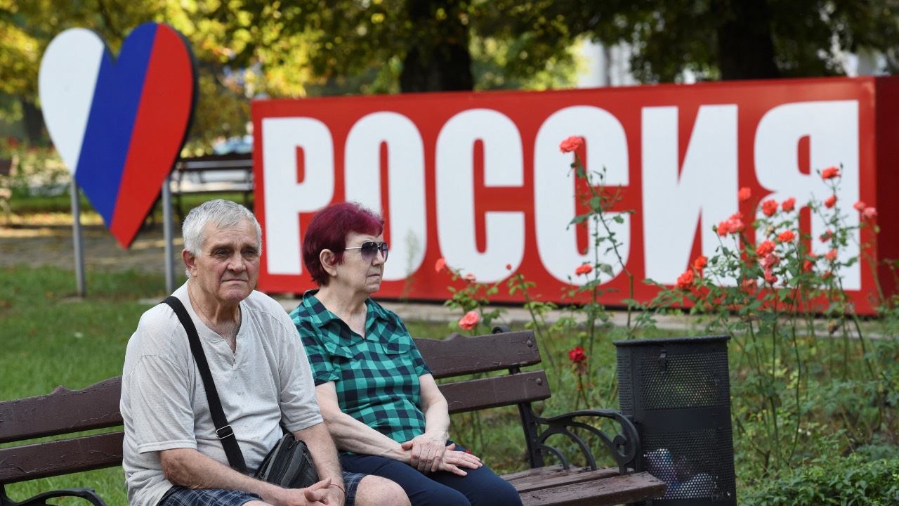 A couple sits on a bench next to a board which reads 'Russia' in central Donetsk, the capital of the self-proclaimed state of the Donetsk People's Republic (DPR) in eastern Ukraine. /STR/AFP