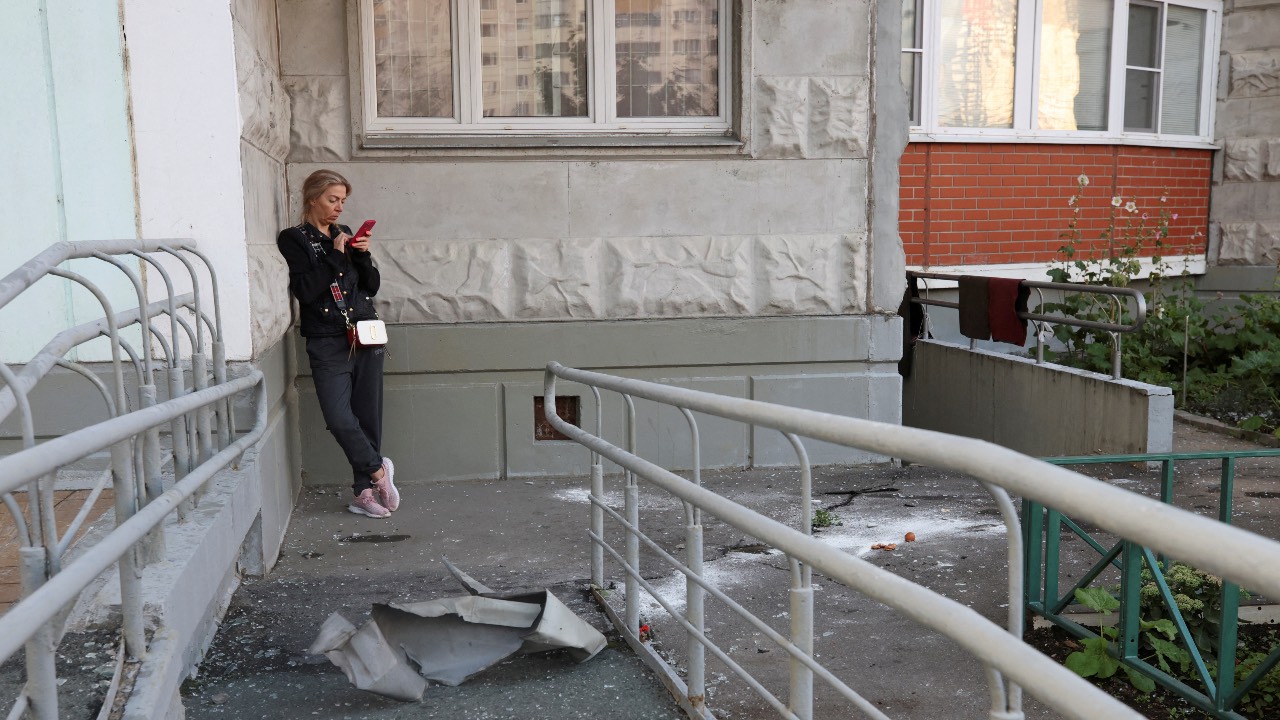 A woman checks her phone next to debris, following a reported drone attack in Krasnogorsk, Russia. /Stringer/Reuters
