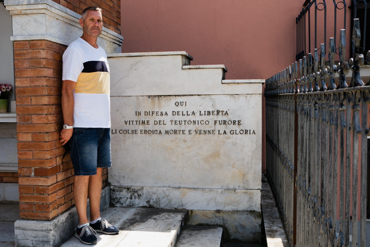 Mauro Petrarca poses for a photo next to a memorial in Fornelli honoring six men, including his great grandfather, hanged by the German army in 1943. The writing reads 'Here in defense of freedom, victims of Teutonic fury heroically met their death, and glory came.' /Crispian Balmer/Reuters