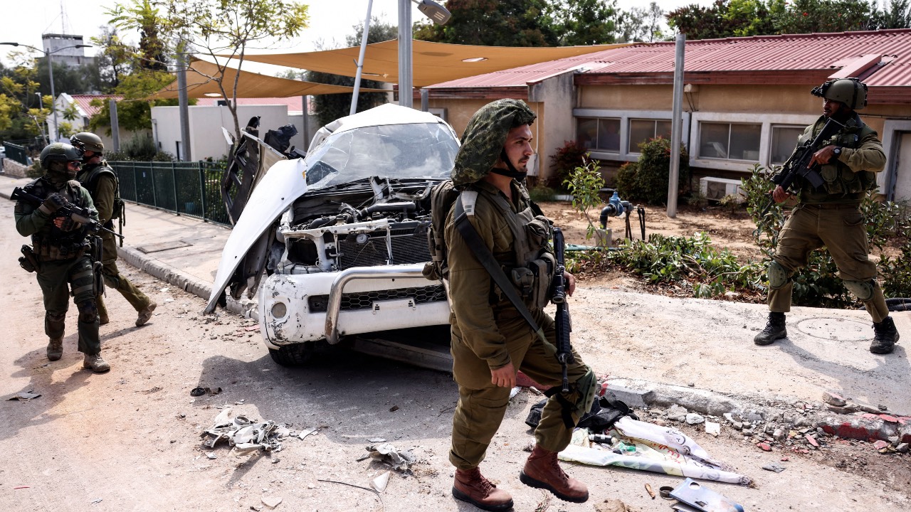 Israeli soldiers walk past a damaged car in Kibbutz Kfar Aza, in southern Israel. /Ronen Zvulun/Reuters