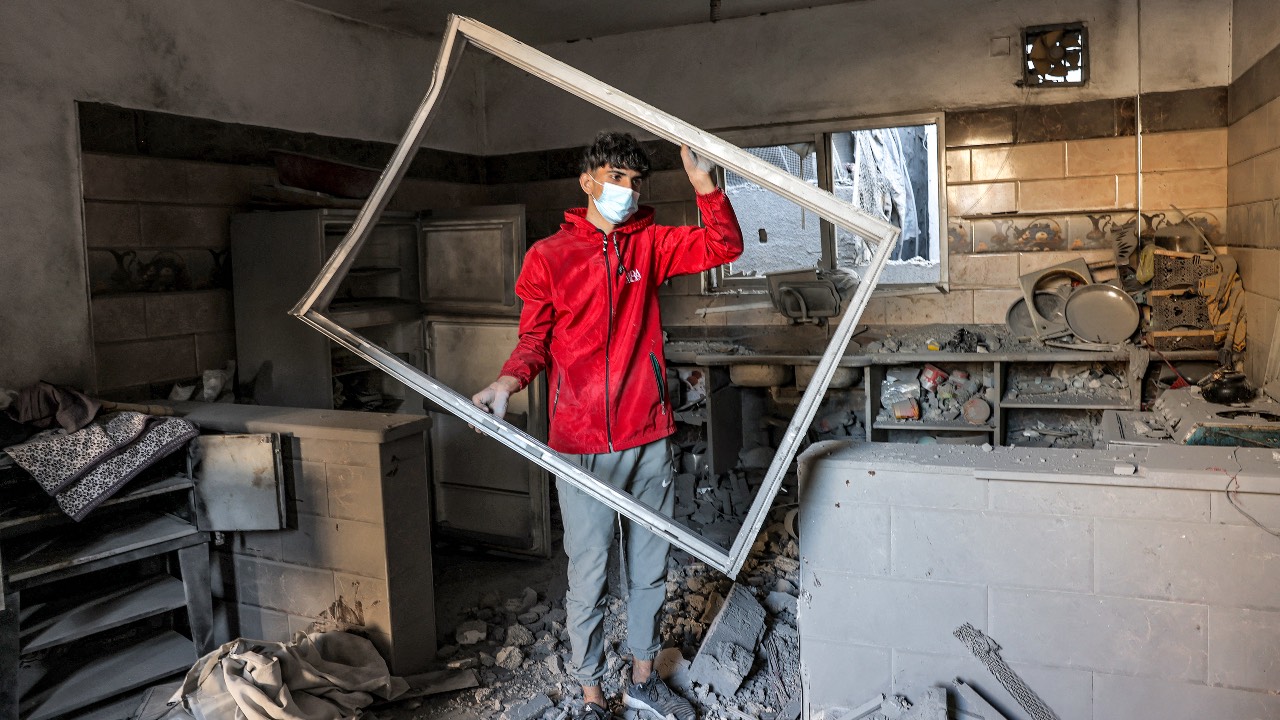 A young man holds a damaged window frame while standing amidst rubble in a kitchen in a building hit by Israeli bombardment in Rafah in the southern Gaza Strip. /Mohammed Abed/AFP