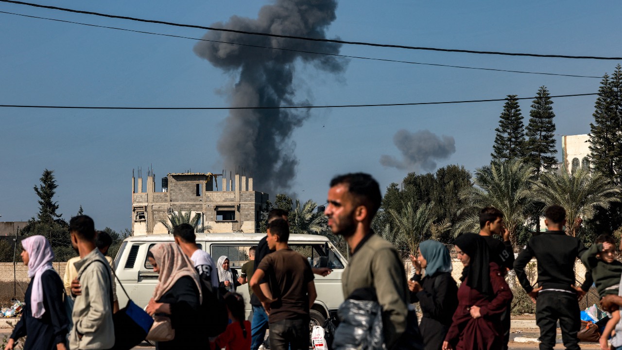 Smoke from Israeli bombardment rises behind people fleeing Gaza City and other parts of the northern Gaza Strip towards the south of the Palestinian enclave as they walk along a highway. /Mohammed Abed/AFP