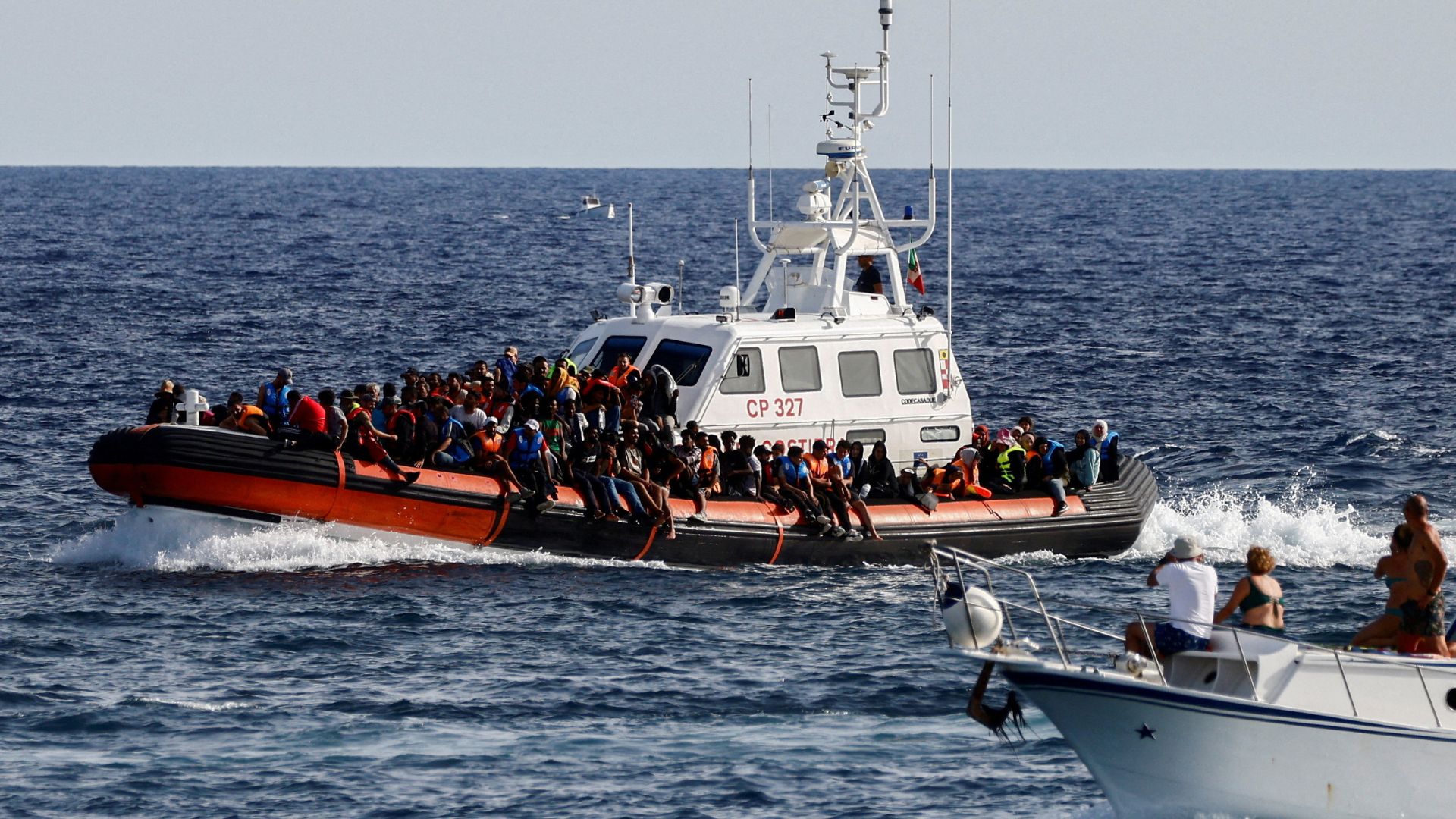 An Italian Coast Guard vessel carrying migrants rescued at sea passes near a tourist boat off Lampedusa in September. /Yara Nardi/Reuters