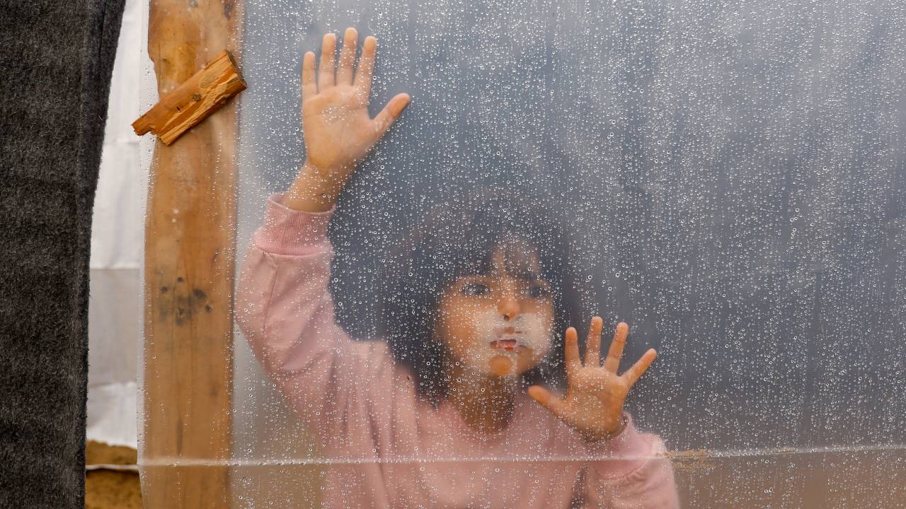 A displaced Palestinian girl looks through a plastic sheet covering a shelter at a tent camp, following rainfall in Khan Younis in the southern Gaza Strip. /Ibraheem Abu Mustafa/ Reuters