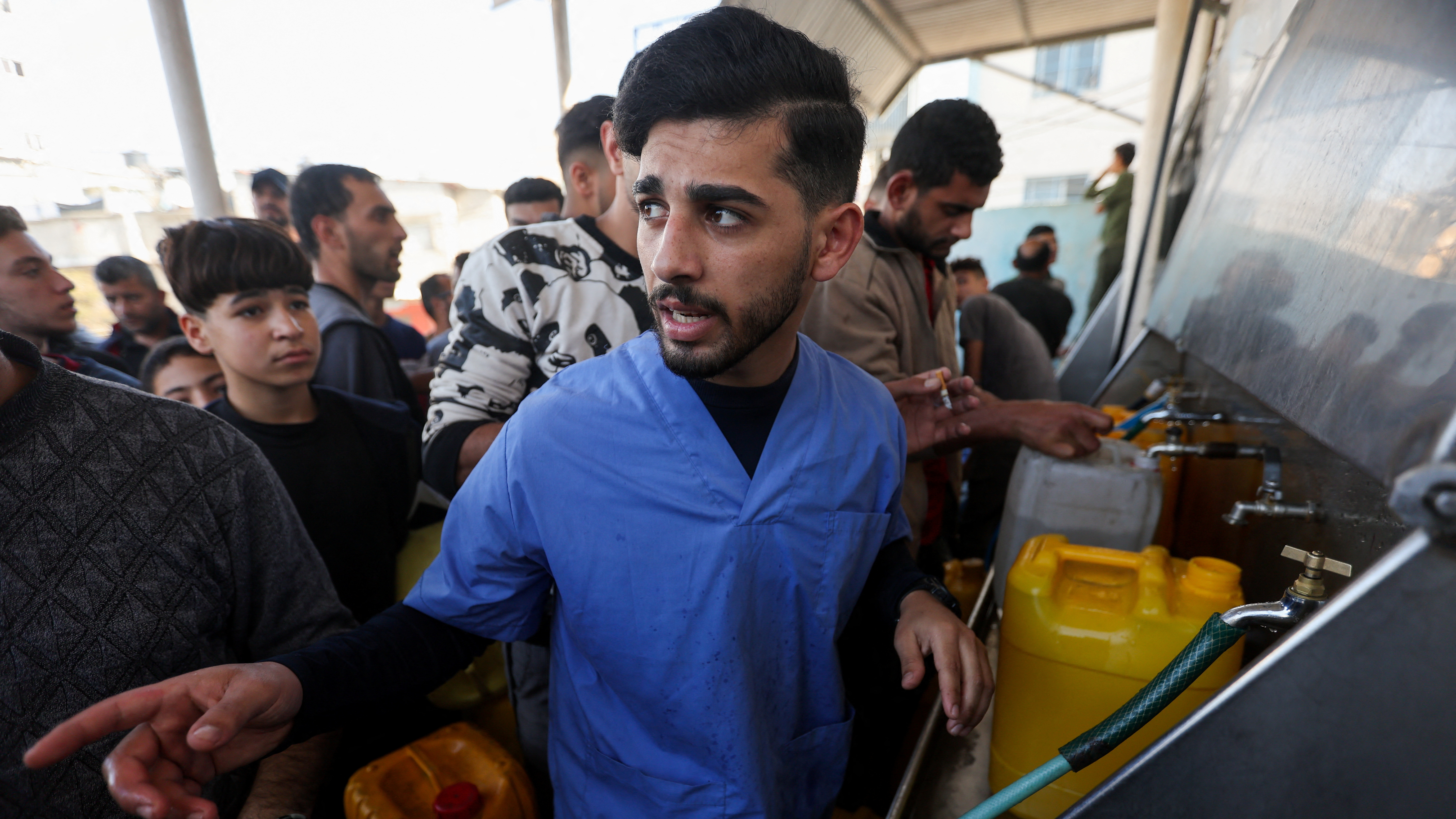 Mahmoud Hisham Abu Lamdi, a 23-year-old nurse displaced from Al-Shati refugee camp in the north of Gaza, stands by taps with water after waiting in a queue to fill a container in the southern city of Khan Younis. /Ibraheem Abu Mustafa/Reuters
