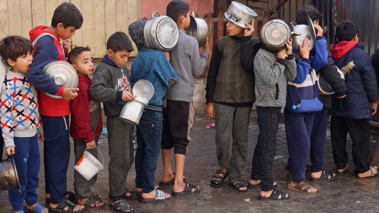 Palestinian children hold pots as they queue to receive food cooked by a charity kitchen in Rafah in the southern Gaza Strip. /Saleh Salem/Reuters