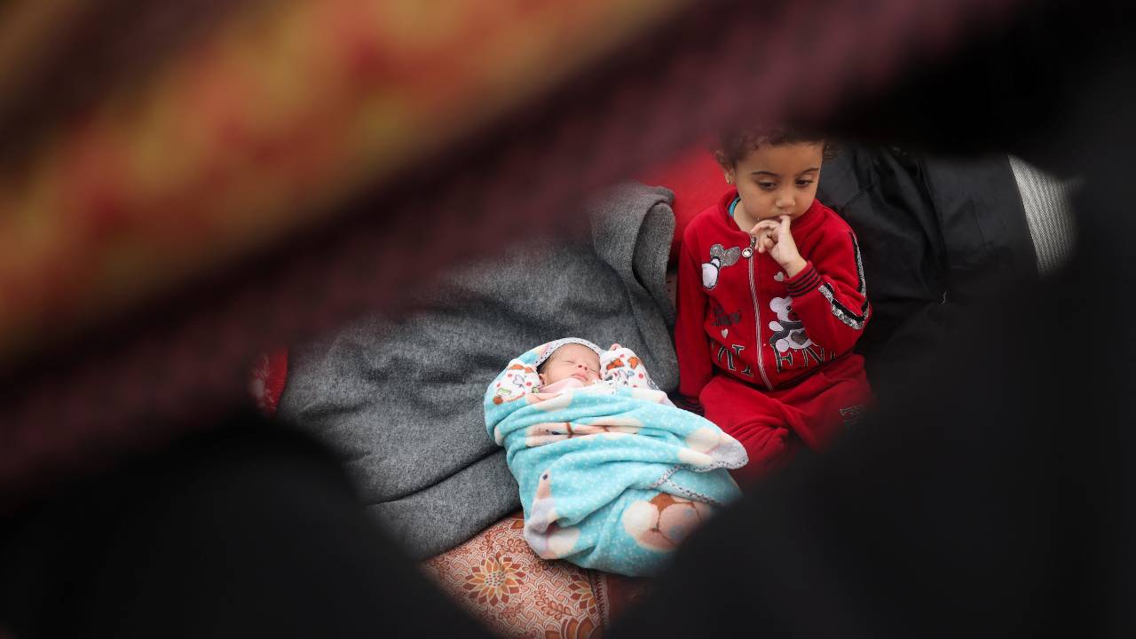 A girl sits next to Alma Al-Jadba, a twin Palestinian baby girl who was war born during the war, in a tent where they shelter with their displaced family who fled their house due to Israeli strikes. /Saleh Salem/Reuters