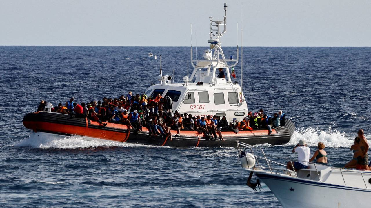 An Italian Coast Guard vessel carrying migrants rescued at sea passes near a tourist boat on the Italian island of Lampedusa. /Yara Nardi/Reuters