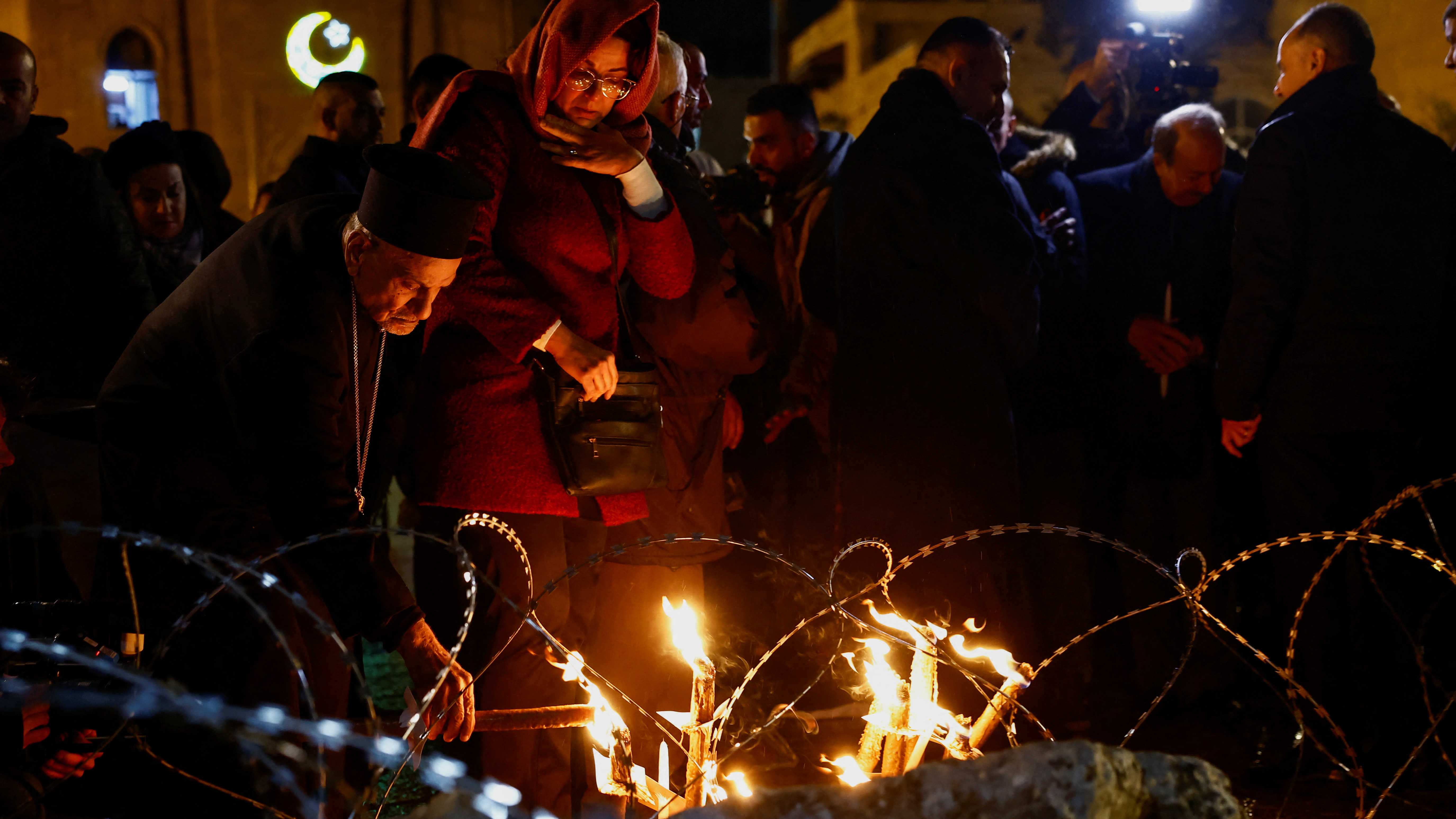 A priest lights a candle at a Christmas installation of a grotto with figures amid rubble surrounded by a razor wire, outside the Church of the Nativity, Bethlehem. REUTERS/C Kilcoyne