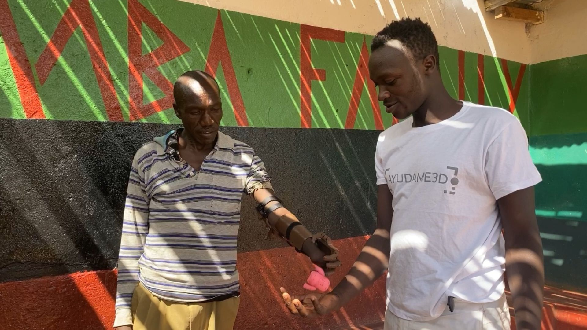 Nelson from Ayudame 3D's Kenyan lab shows a recipient how to open and close the fingers on his new prosthetic arm.  /Handout