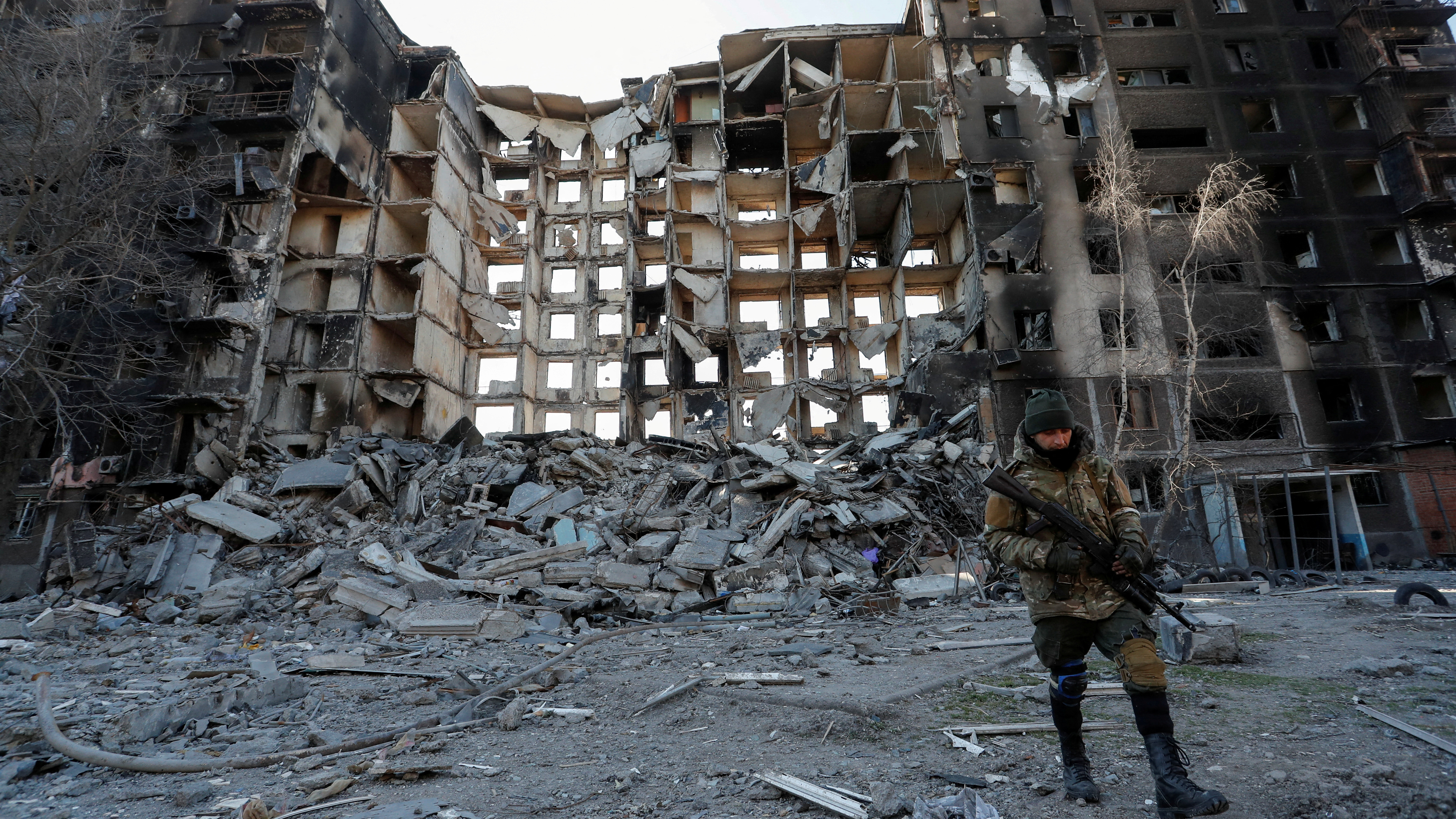 Russian troops walk near an apartment building destroyed in the course of Ukraine-Russia conflict in the besieged southern port city of Mariupol, Ukraine./Alexander Ermochenko/Reuters 