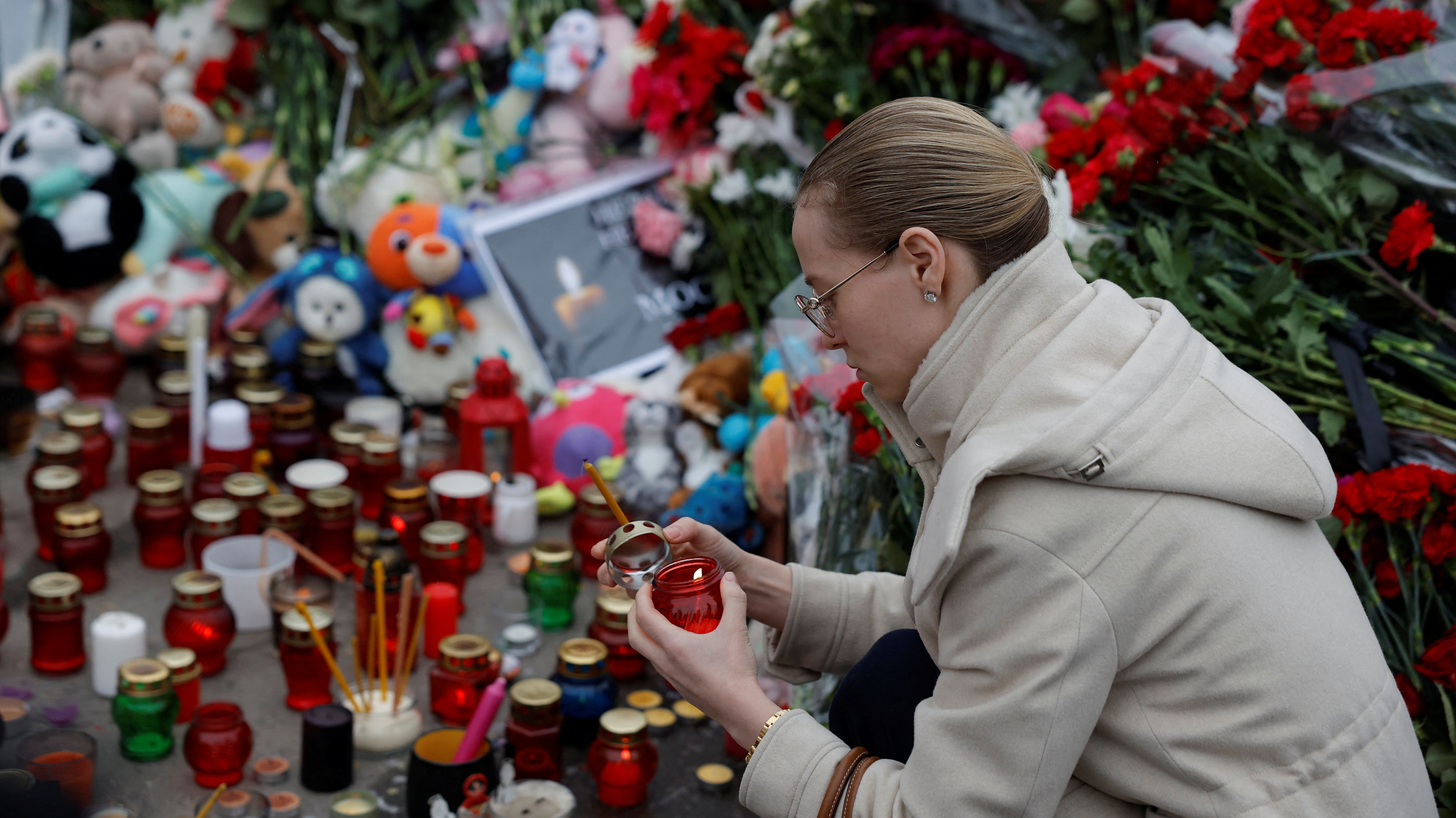 A woman lights a candle at a makeshift memorial to the victims of a shooting attack set up outside the Crocus City Hall concert venue. /Maxim Shemetov/Reuters