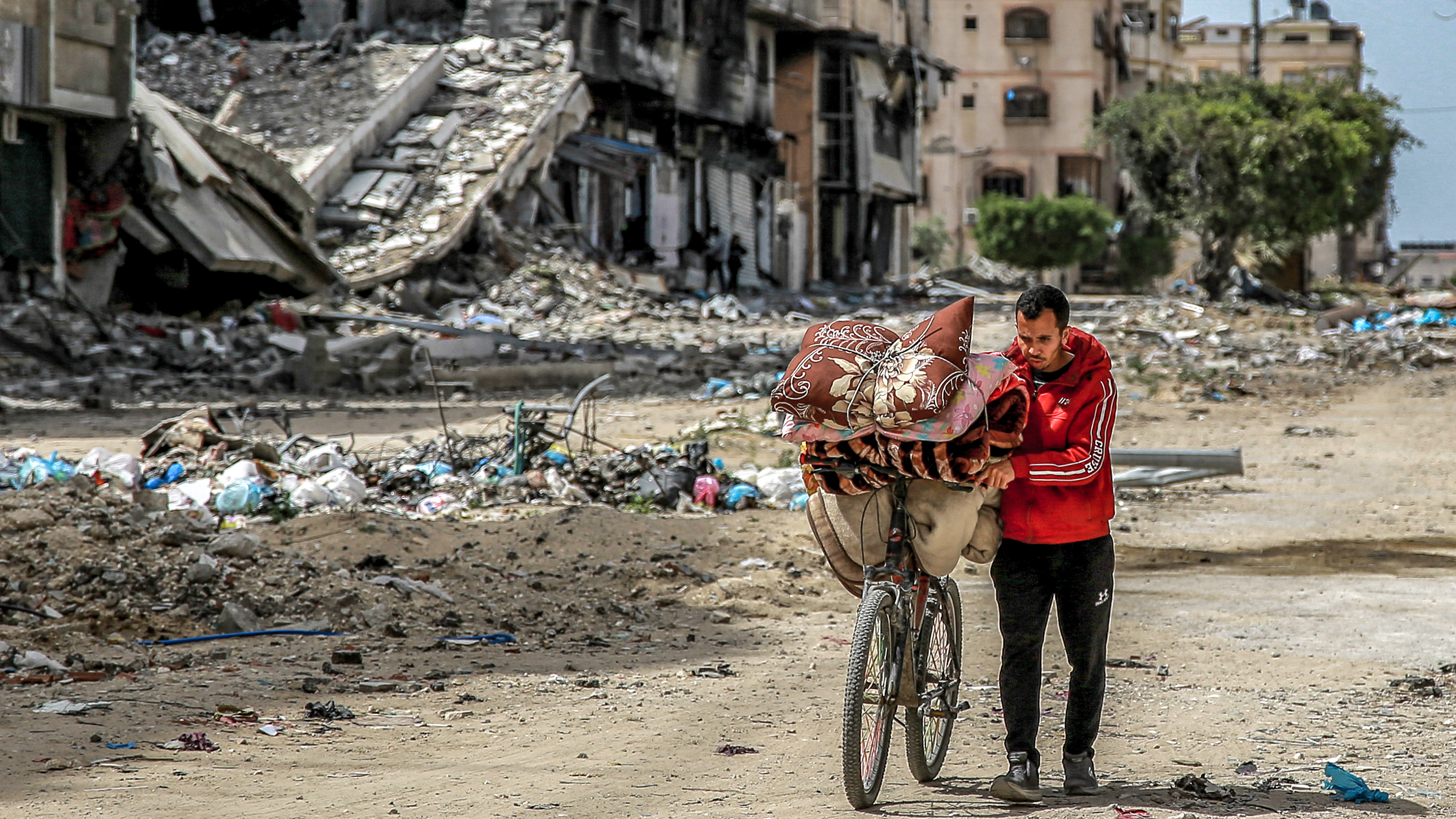 A man walks with a bicycle loaded with blankets and cushions past destroyed buildings. /AFP