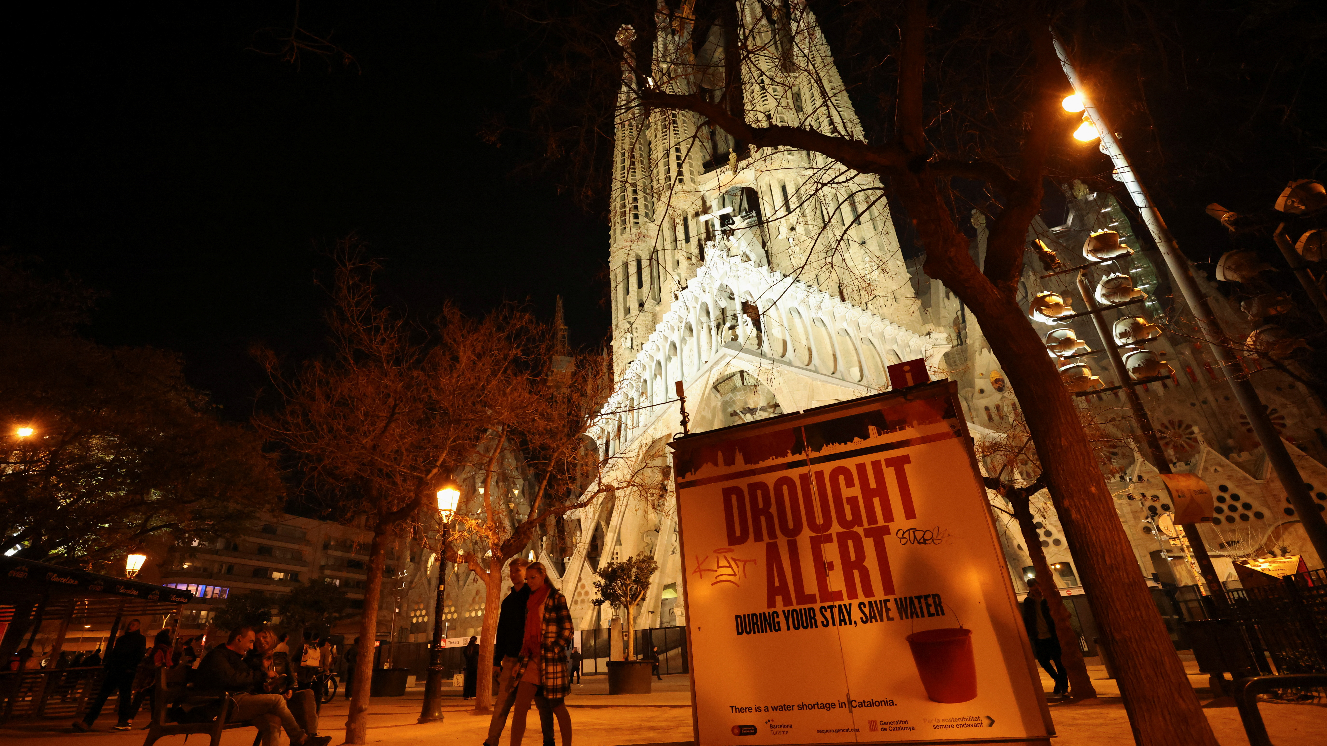 Tourists walk past a sign at Sagrada Familia Basilica alerting them of severe drought in Spain's northeastern region and urging them to save water./Nacho Doce/Reuters