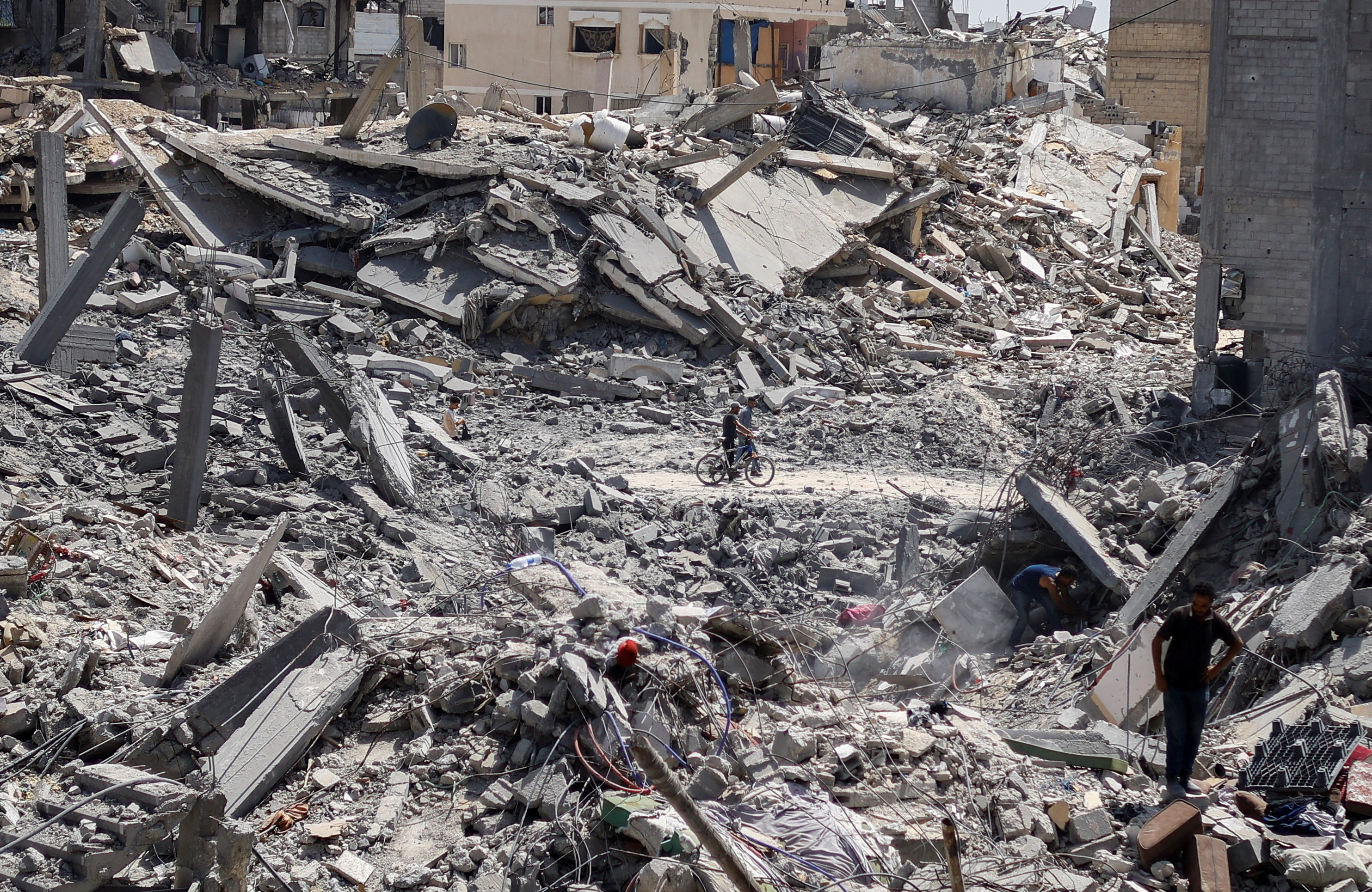 Palestinians walk past the rubble as other search for belongings in the aftermath of an Israeli strike, in Khan Younis. /Mohammed Salem/Reuters