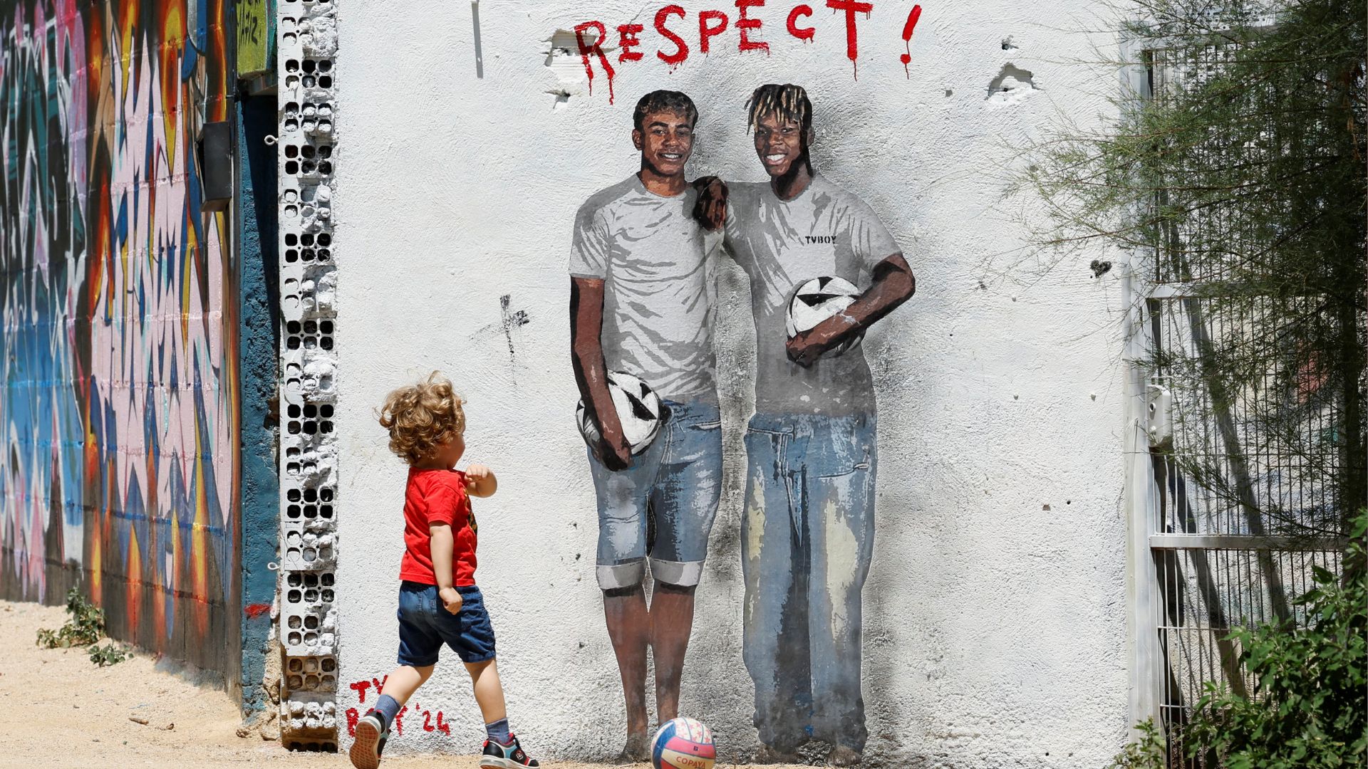 A young boy plays football in front of a mural of Spanish footballers, Lamine Yamal and Nico Williams./Albert Gea/Reuters