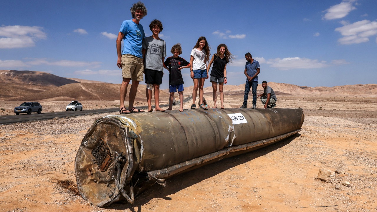 People stand on top of the remains of an Iranian missile in the Negev desert near Arad, in the aftermath of an Iranian missile attack on Israel. /Menahem Kahana/AFP