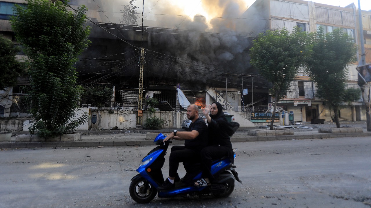 A man on a scooter drives past a building set ablaze by an Israeli strike that targeted the Sfeir neighborhood in Beirut's southern suburbs. /AFP