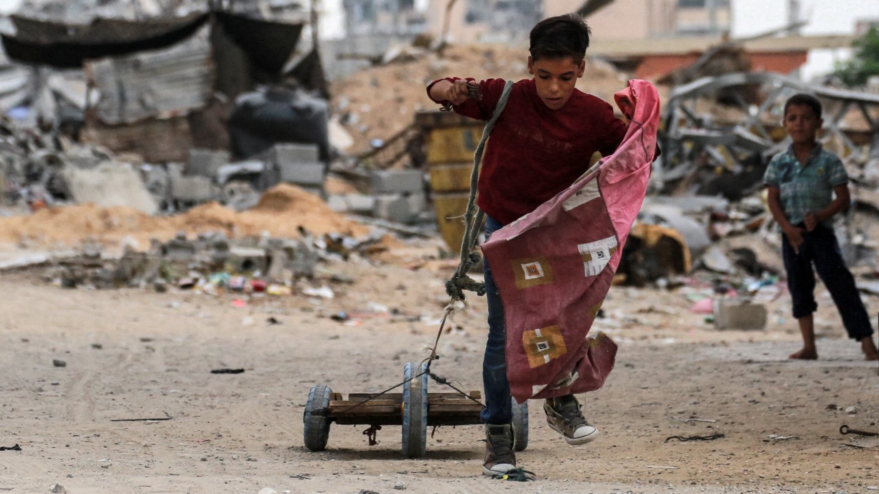 A boy pulls a cart with a rope while walking past a destroyed building in Khan Yunis. /Bashar Taleb/AFP