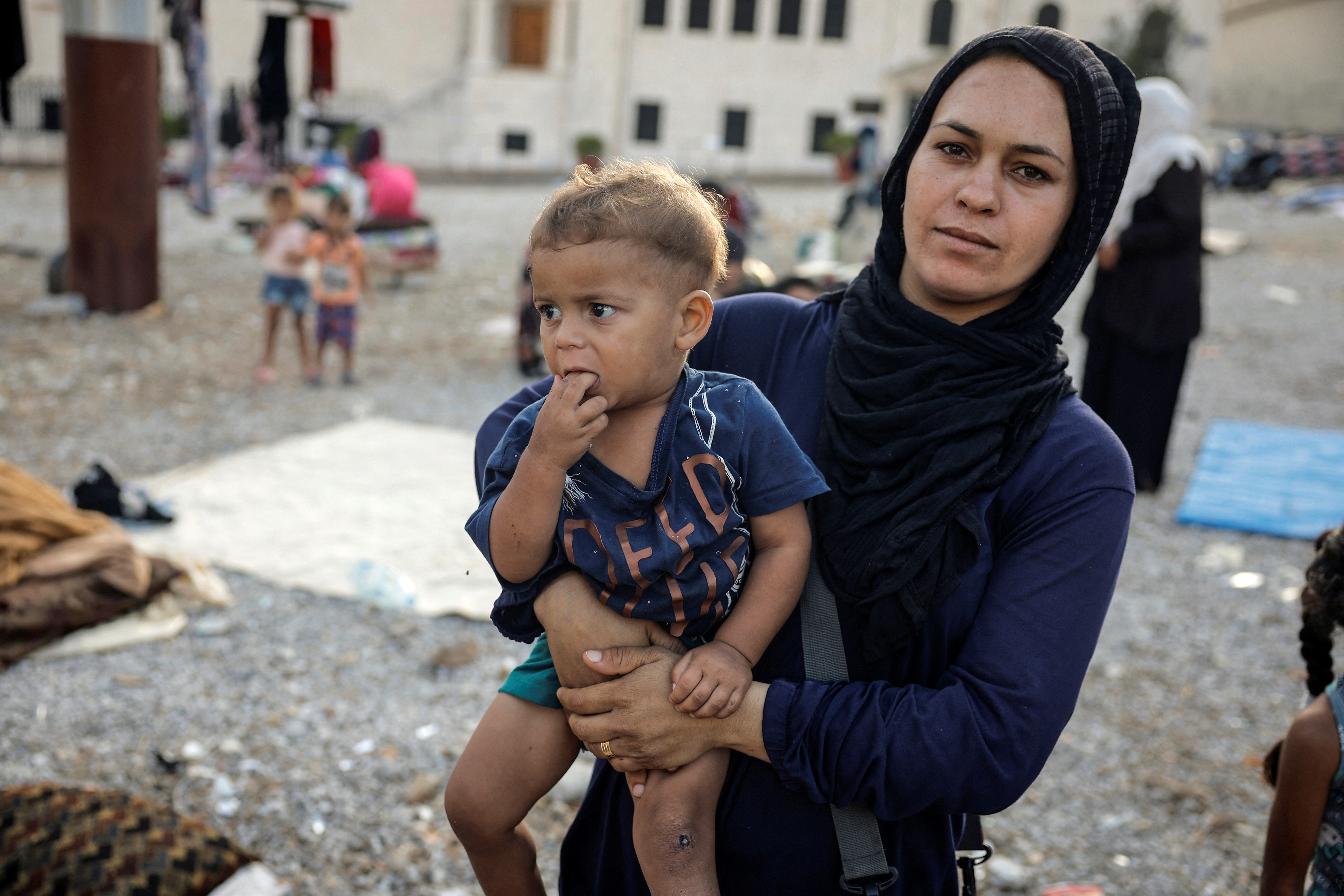 A displaced woman holds her child at a gravel lot, where families have taken temporary shelter, amid the ongoing hostilities, in Beirut, Lebanon, /Louisa Gouliamaki/Reuters