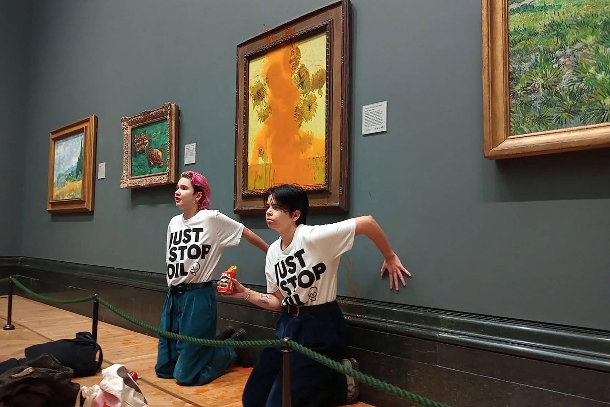 Activists from the Just Stop Oil climate campaign glue their hands to the wall after pouring soup on Vincent Van Gogh's painting 'Sunflowers' at the National Gallery. /Just Stop Oil/AFP
