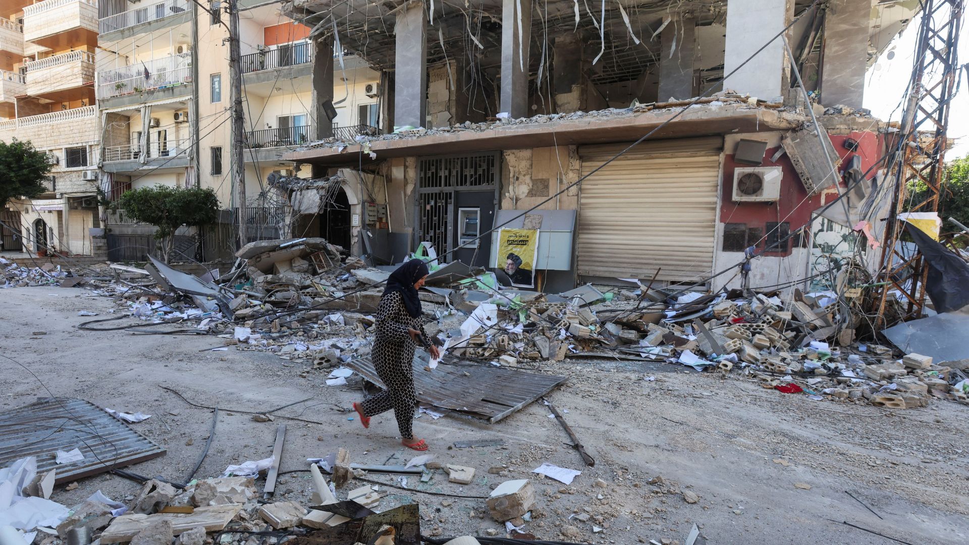 A woman in Tyre, Lebanon, walks past a damaged branch of Al-Qard al-Hassan, a financial institution Israel says is linked to Hezbollah. /Aziz Taher/Reuters